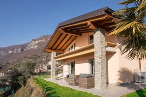 A modern house with a stone facade, a wooden roof, and a patio with outdoor furniture. - Villa Donagh sleeps 12, lake view & pool by Italian Apartments. (Ossuccio)