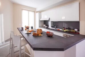 A modern kitchen with white cabinets, a black countertop, and a dining area with white chairs. - Villa Donagh sleeps 12, lake view & pool by Italian Apartments. (Ossuccio)
