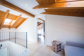 Une chambre spacieuse aménagée en mezzanine, avec un plafond en pente, un escalier en bois et une vue sur le salon attenant.