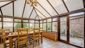 Ein Wintergarten mit Holztisch und -stühlen, großen Fenstern und einer Ziegelwand im Außenbereich.