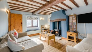 Ein gemütliches Wohnzimmer mit Kamin, Holzbalken, einer Couch, einem Couchtisch und einem Bücherregal.