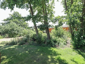 A garden with trees and shrubs, a wooden fence, and a building in the background. - 80 Pentney Lakes (King's Lynn)