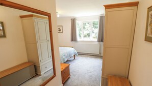 Une chambre à coucher avec un lit, une armoire, un miroir, un radiateur et une fenêtre avec des rideaux.