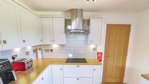 Une cuisine avec des meubles blancs, un plan de travail en bois, un grille-pain rouge, une cuisinière et une porte.