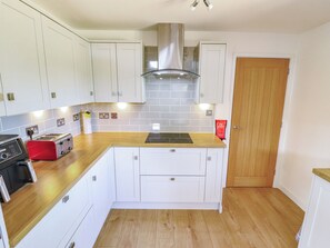 A kitchen with white cabinets, a wooden countertop, a red toaster, a stove, and a door. - 80 Pentney Lakes (King's Lynn)