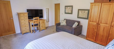 A bedroom with a bed, a desk with a chair, a television, a wardrobe, and two framed pictures on the wall.