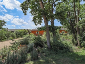 A rural setting with two red-roofed buildings surrounded by dense vegetation and trees. - 80 Pentney Lakes (King's Lynn)