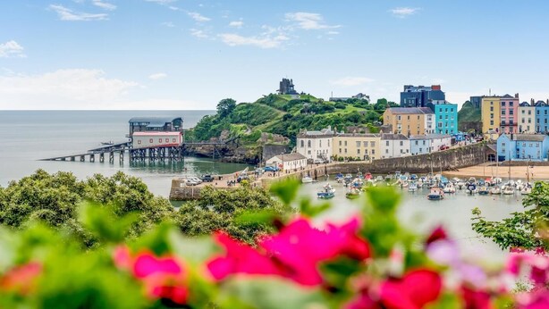 A coastal town with colorful buildings, a pier, and a hill with a castle-like structure. - 1 Bed in Tenby (oc-t36054) (Tenby)