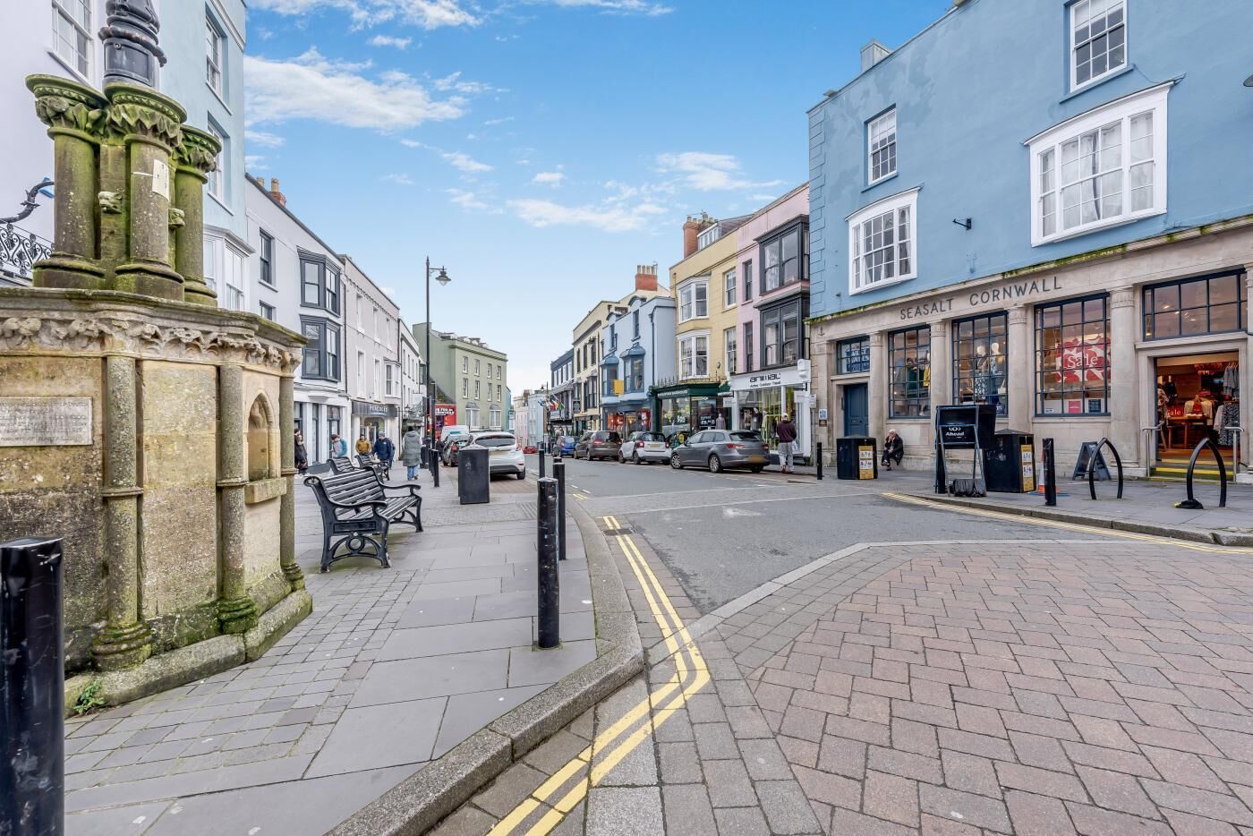 A street with shops, a stone monument, and a pedestrian walkway.