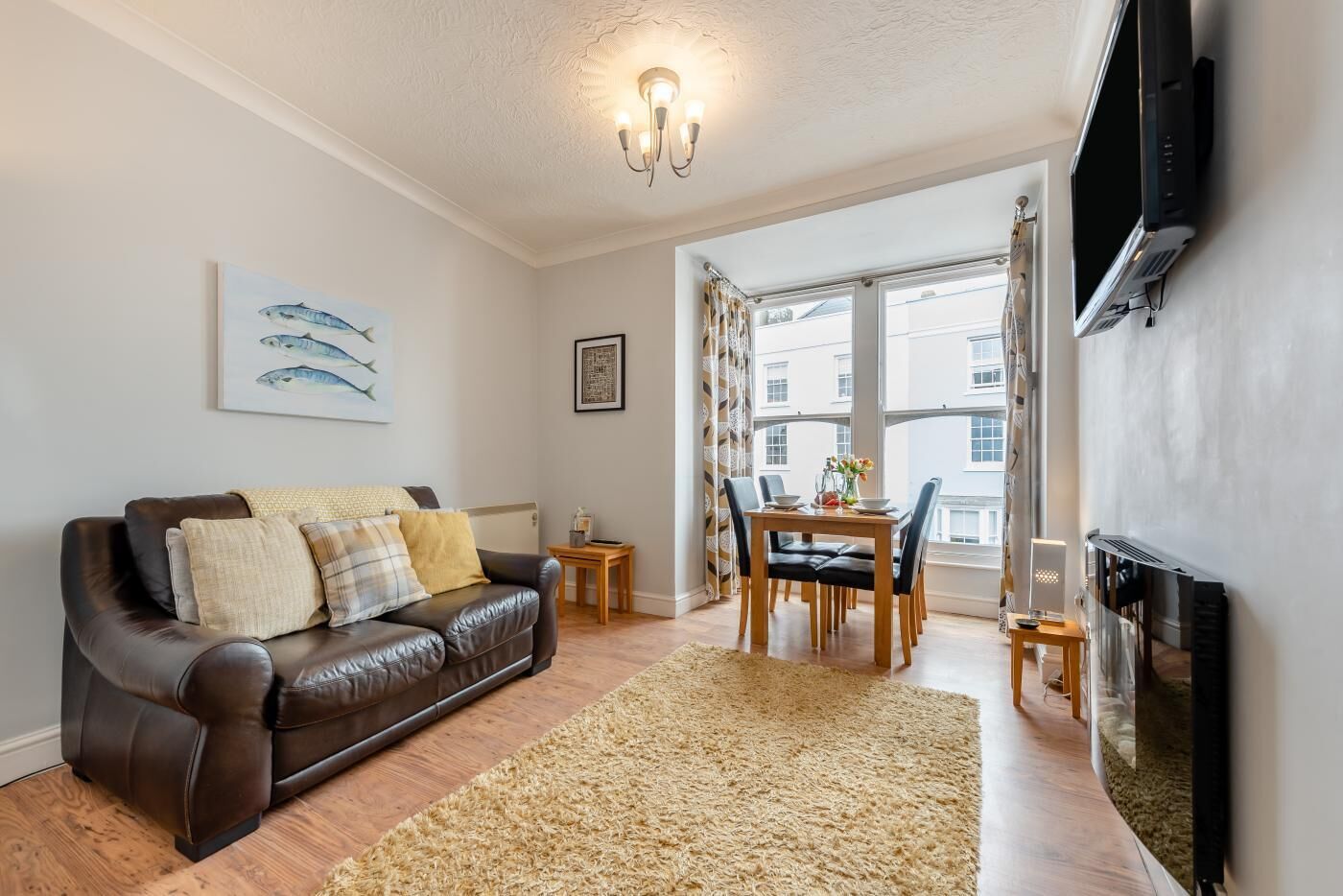 A living room with a leather sofa, a dining table with chairs, a fireplace, and a TV mounted on the wall.