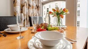 A dining table set with plates, glasses, bread, grapes, and a vase of flowers. - 1 Bed in Tenby (oc-t36054) (Tenby)