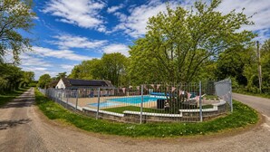 Een omheind zwembad met een huis en bomen op de achtergrond.