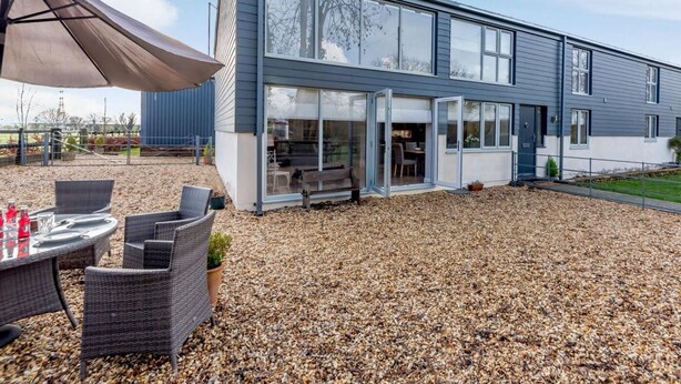 Een modern gebouw met twee verdiepingen, grote ramen, een overdekt terras met tuinmeubilair en een grindpad.