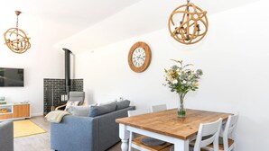 Uma sala de estar moderna com sofá, mesa de jantar com cadeiras, lareira, relógio de parede e luminária pendente.