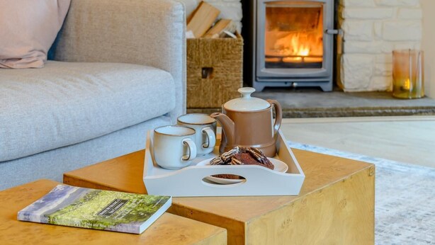 Ein gemütliches Wohnzimmer mit einer Couch, einem Couchtisch mit Tassen, einem Buch und einem Kamin.