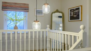 Eine Treppe mit weißen Balustern und einem weißen Geländer, eine hängende Leuchte, ein Fenster mit Blick auf Bäume und ein gerahmtes Bild an der Wand.