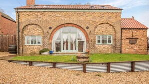 A brick house with a tiled roof, a large arched window, and a small garden area with gravel and plants. - 2 Bed in Belchford (oc-o36036) (Belchford)