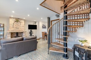 Ein modernes Wohnzimmer mit Kamin, einer Couch, einer Treppe mit freiliegenden Rohren und einem wandmontierten Flachbildfernseher.