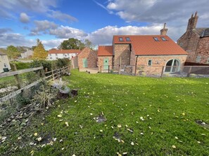 Ein Haus aus Backsteinen mit rotem Ziegeldach, einem umzäunten Garten und einer grünen Tür.