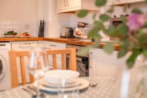 Eine Küche mit Holzarbeitsplatte, einem Toaster, einer Waschmaschine und einem Esstisch mit Blumen in einer Vase.