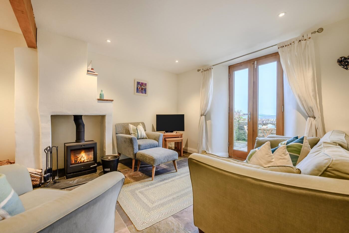 A cozy living room with a fireplace, a sofa, a chair, a TV, and a view through a glass door.