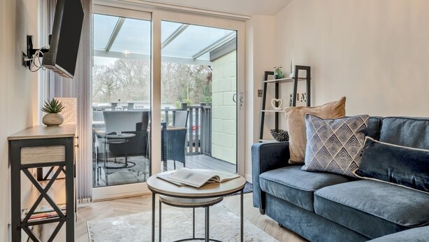 Ein modernes Wohnzimmer mit einer Couch, einem kleinen Tisch, einem Fernseher und einer Schiebeglastür, die auf eine Außenpatio führt.