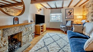 A cozy living room with a stone fireplace, wooden beams, a television, a plaid armchair, and a view through a window. - 2 Bed in Whitby (oc-dedi4) (Whitby)