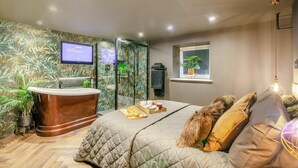 Ein modernes Hotelzimmer mit einem großen Bett, einem Holzbüro, einem Fernseher und einem Fenster mit Pflanze.