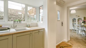 A kitchen with a sink, countertop, and cabinets. There is a window with a view of a brick wall and a fence. A door leads to a dining area with a table and chairs. - 2 Bed in Snettisham (oc-k36331) (Snettisham)