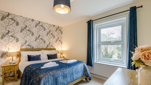 A bedroom with a bed, bedside lamps, a window with curtains, and a vase with flowers. - 2 Bed in Snettisham (oc-k36331) (Snettisham)