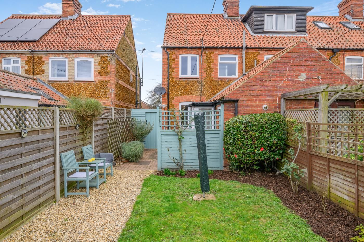 A residential area with terraced houses, a fenced garden, and a seating area with chairs.