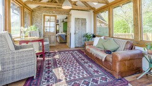 A cozy room with a wooden ceiling, a brown leather sofa, a wicker chair, and a patterned rug. - 1 Bed in Picklescott (oc-o35147) (Ratlinghope)