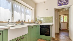 A kitchen with green cabinets, a sink, a stove, and a window with curtains. - 1 Bed in Picklescott (oc-o35147) (Ratlinghope)