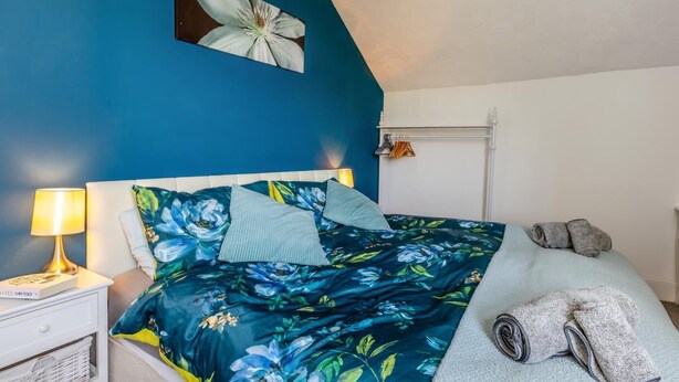 A bedroom with a bed, pillows, a nightstand, a lamp, a framed picture, and a radiator. - 4 Bed in Mortehoe (oc-d35057) (Mortehoe)