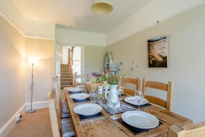 A dining area with a wooden table set for four, a vase of flowers, and a painting on the wall.