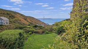 A coastal landscape with a grassy area, a stone tower, and a building with a pitched roof. - 4 Bed in Mortehoe (oc-d35057) (Mortehoe)