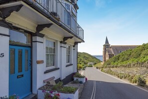 A coastal building with a blue door, white walls, and a balcony.