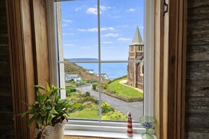 A window with a view of a coastal landscape, including a church and houses. - 4 Bed in Mortehoe (oc-d35057) (Mortehoe)