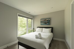A bedroom with a bed, a window, and a painting on the wall.