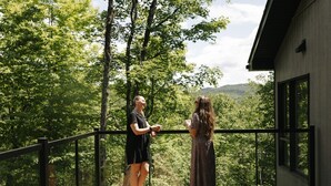 A balcony with a wooden floor, metal railing, and a view of a forested landscape. - Forest immersion | 5 min beach • 15 min Tremblant (Les Laurentides Regional County Municipality)