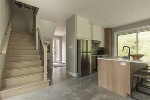 A modern kitchen with a central island, stainless steel appliances, and a staircase leading to another level.