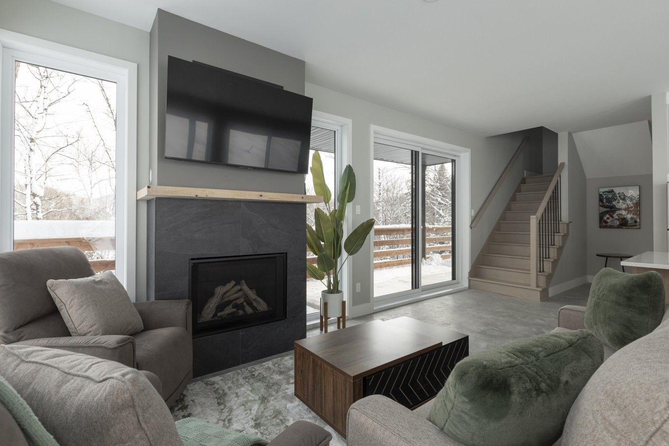 Una sala de estar moderna con chimenea, ventanas amplias y una escalera.