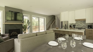 A modern kitchen with a large island, a fireplace, and a dining area set for a meal. - Forest immersion | 5 min beach • 15 min Tremblant (Les Laurentides Regional County Municipality)