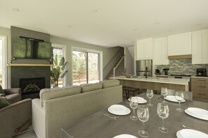 A modern kitchen with a large island, a fireplace, and a dining area set for a meal. - Forest immersion | 5 min beach • 15 min Tremblant (Les Laurentides Regional County Municipality)