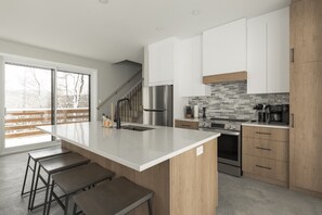 A modern kitchen with a large island, stainless steel appliances, and a view through a sliding door.