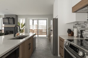 A modern kitchen with a large island, stainless steel appliances, and a sliding glass door leading to a balcony.