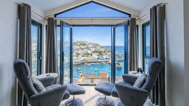 A modern room with a large glass door leading to a balcony overlooking a harbor and town. - 4 Bed in Brixham (oc-t35056) (Brixham)