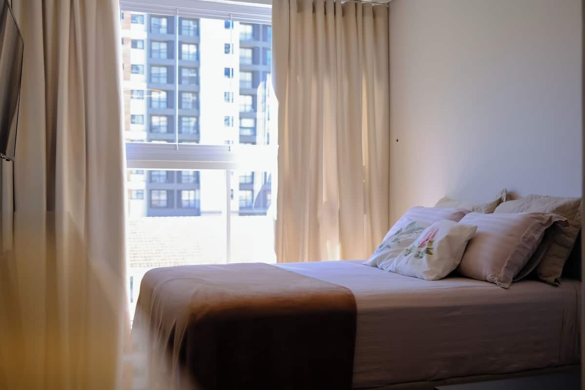 A bedroom with a bed, curtains, and a view of a building through the window.