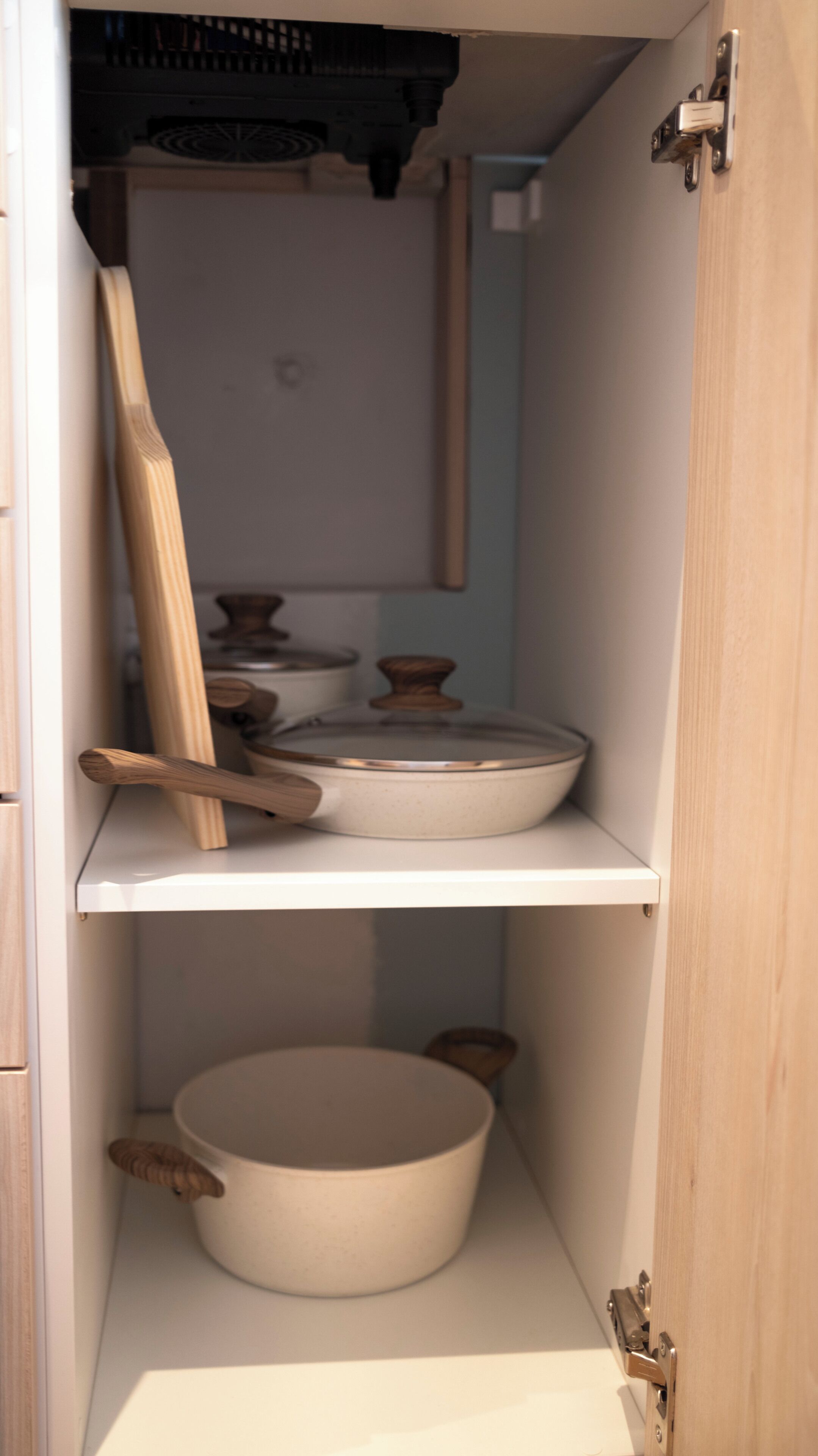 A kitchen cabinet with shelves holding cookware and wooden utensils.