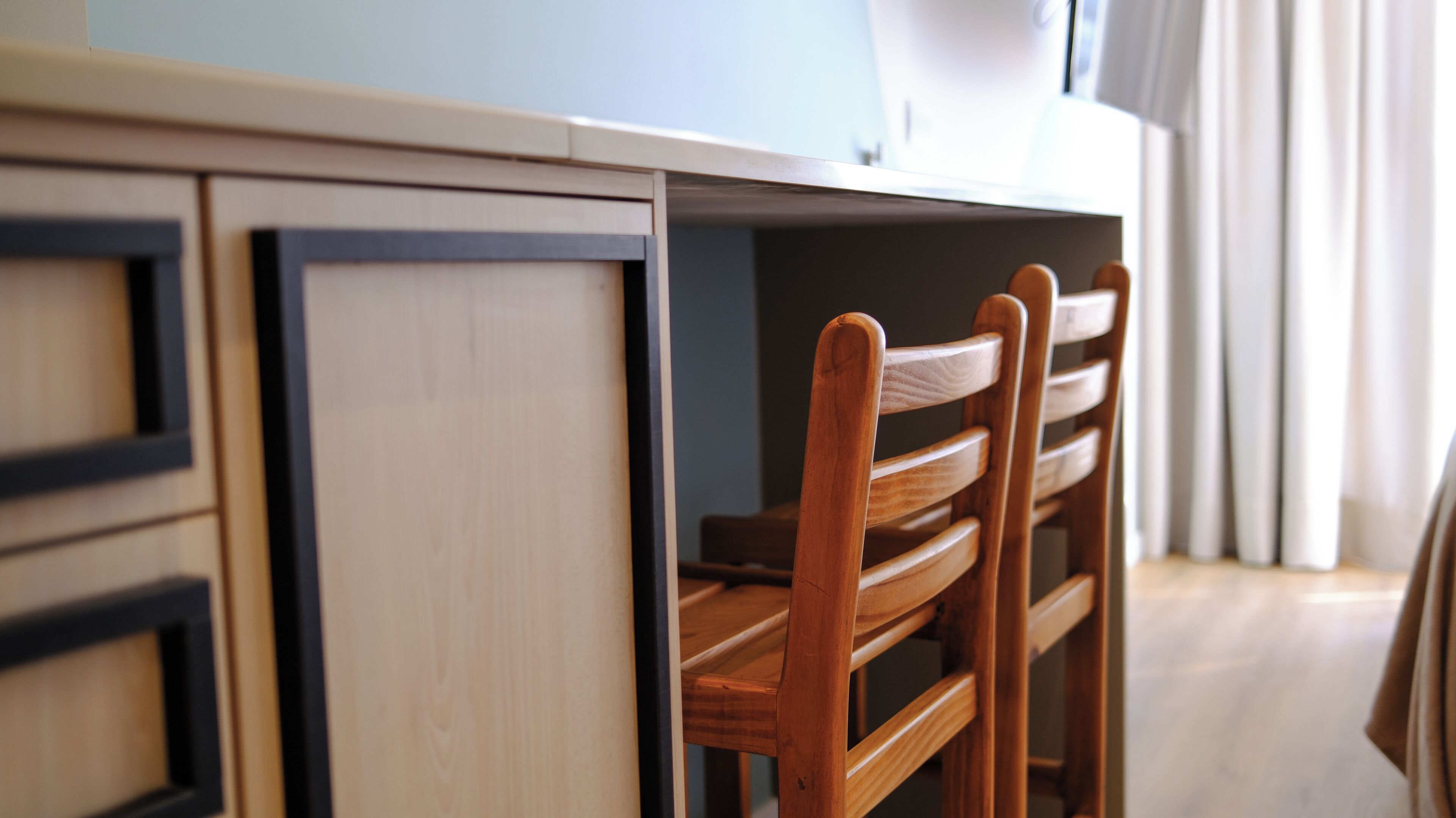 A wooden chair with a backrest and armrests, positioned in front of a kitchen counter with cabinets.